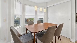 A dining area with a wooden table and six chairs, large windows with blinds, and a hanging light fixture. - Bright Home w/ Patio + Fenced Yard - Sleeps 8 (Galloway)