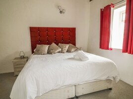 Una cama con cabecera roja, ropa de cama blanca y una mesita de noche con lámpara.