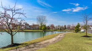 Um parque à beira do lago com uma trilha para pedestres, árvores e casas ao fundo.