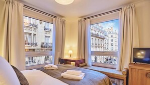 Une chambre d’hôtel équipée d’un lit, d’un bureau, d’une télévision et de grandes fenêtres donnant sur la ville.