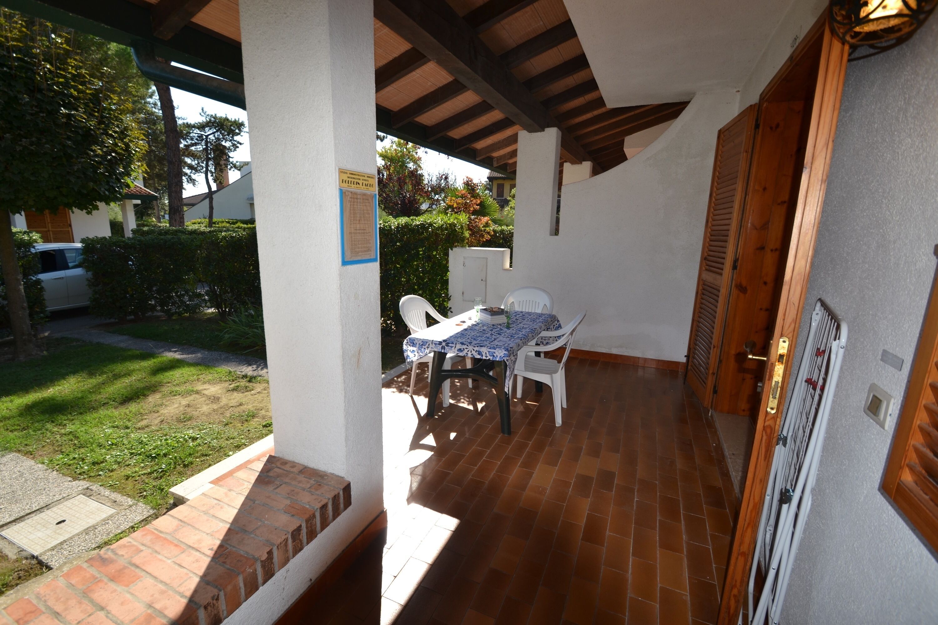 A covered patio with a table and chairs, a brick floor, and a door with a wooden shutter.
