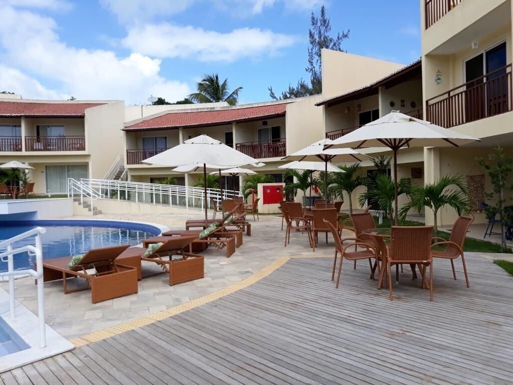 A poolside area with lounge chairs and umbrellas, a pool, and a building with balconies.