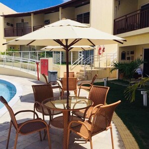 A poolside area with wicker furniture and a large umbrella. - Solar Condominium Agua Pipa by Carpediem (Tibau do Sul)