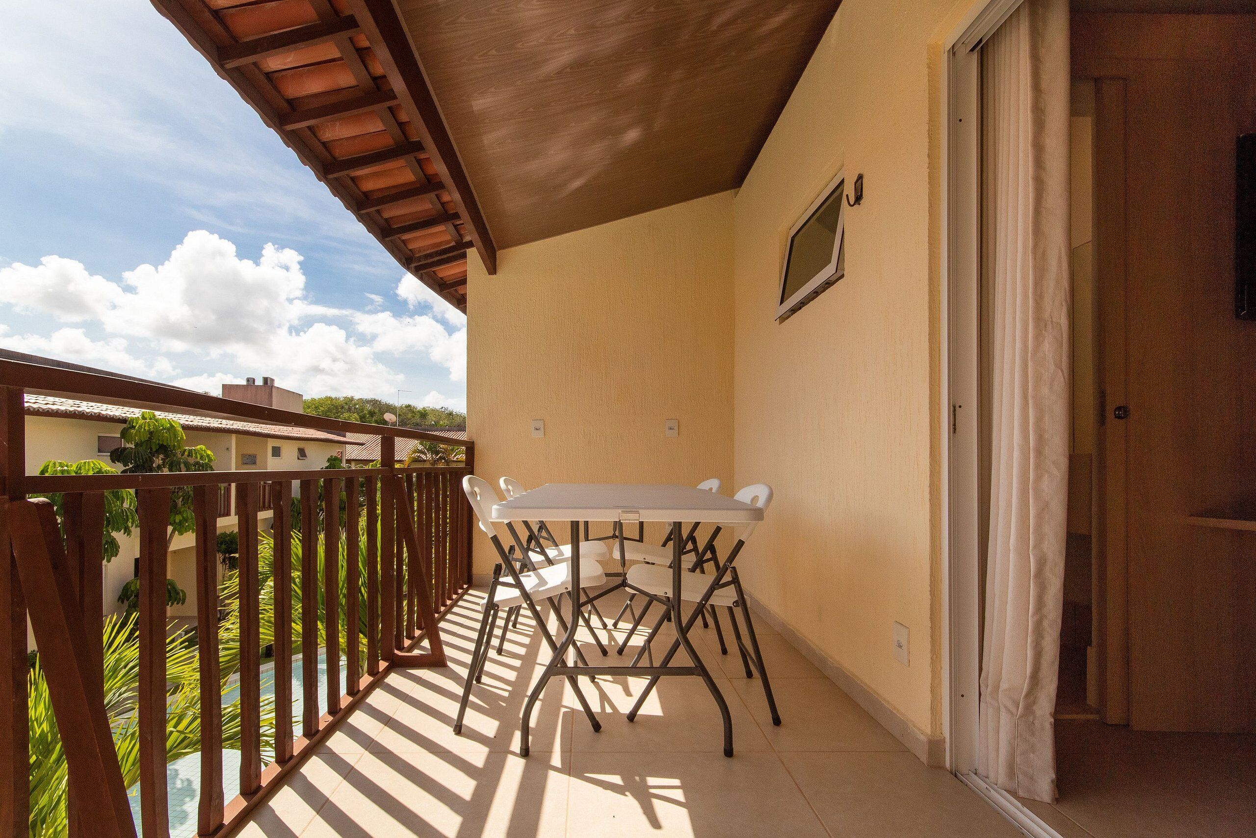 A balcony with a table and chairs, a wooden railing, and a door leading to an interior space.