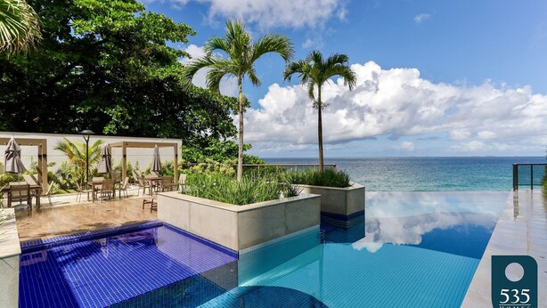 Ein Infinity-Pool mit freiem Blick auf den Ozean, umgeben von Palmen und Liegestühlen.