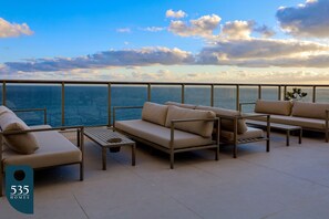 Una terraza con un sofá, sillones y una pequeña mesa, con vista a una masa de agua.