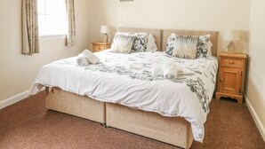 Uma cama bem arrumada com roupa de cama florida, duas mesas de cabeceira com luminárias e três quadros na parede.