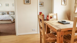 Um quarto com uma mesa de jantar de madeira, cadeiras e uma cama com cabeceira bege.