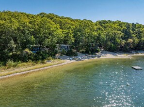 Una propiedad frente al lago con una casa rodeada de bosque denso, una playa de arena y un muelle.