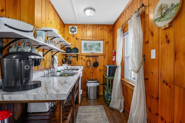 A compact kitchen with wooden walls, a marble countertop, and a window with a view.