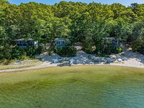 A beachfront property with multiple cabins surrounded by dense forest, a sandy beach, and a clear view of the water.