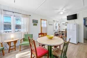 Ein gemütlicher, gut beleuchteter Raum mit einem runden Holztisch, grünen und roten Stühlen, einer gelben Schale und einem weißen Kühlschrank.