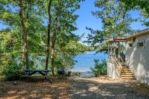 A cabin with a deck, a picnic table, and a view of a lake. - Peaceful Waterfront Cottage with Pond Views (Sandwich)