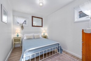 A bedroom with a bed, two bedside tables, a mirror, and a window with curtains. - Peaceful Waterfront Cottage with Pond Views (Sandwich)