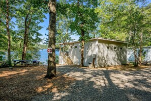 Une cabane dotée d’une terrasse et d’un espace abrité, entourée d’arbres et bordée par un plan d’eau.