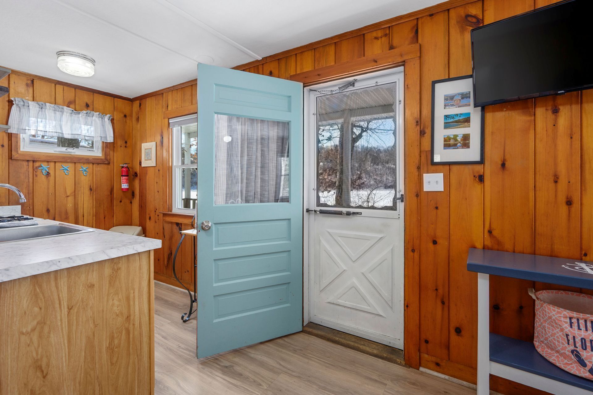 A wooden interior with a kitchen area, a door leading outside, and a mounted television.