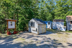 A gravel area with a small shed, a wooden signboard, and a blue container. - Cozy Cape Cod Cottage with Peaceful Water Views (Sandwich)