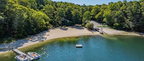 A lakeside property with a dock, a boat, and a sandy beach surrounded by dense trees.