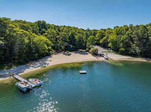 Ein Seeufergrundstück mit Steg, Boot und Sandstrand, umgeben von dichtem Baumbestand.
