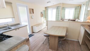 Une cuisine compacte équipée d’une cuisinière, d’un évier et d’un plan de travail en bois. Un coin repas avec une table et des chaises est également prévu.