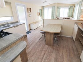 Cocina compacta con estufa, pileta y encimera de madera. Hay un comedor con mesa y sillas.