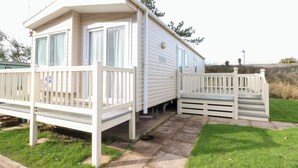 Une maison mobile dotée d’un porche et d’une terrasse délimitée par une clôture.