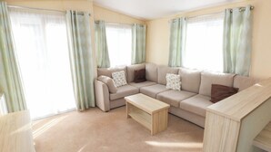 Un salon spacieux avec un canapé d’angle beige, une table basse en bois et des rideaux vert clair.