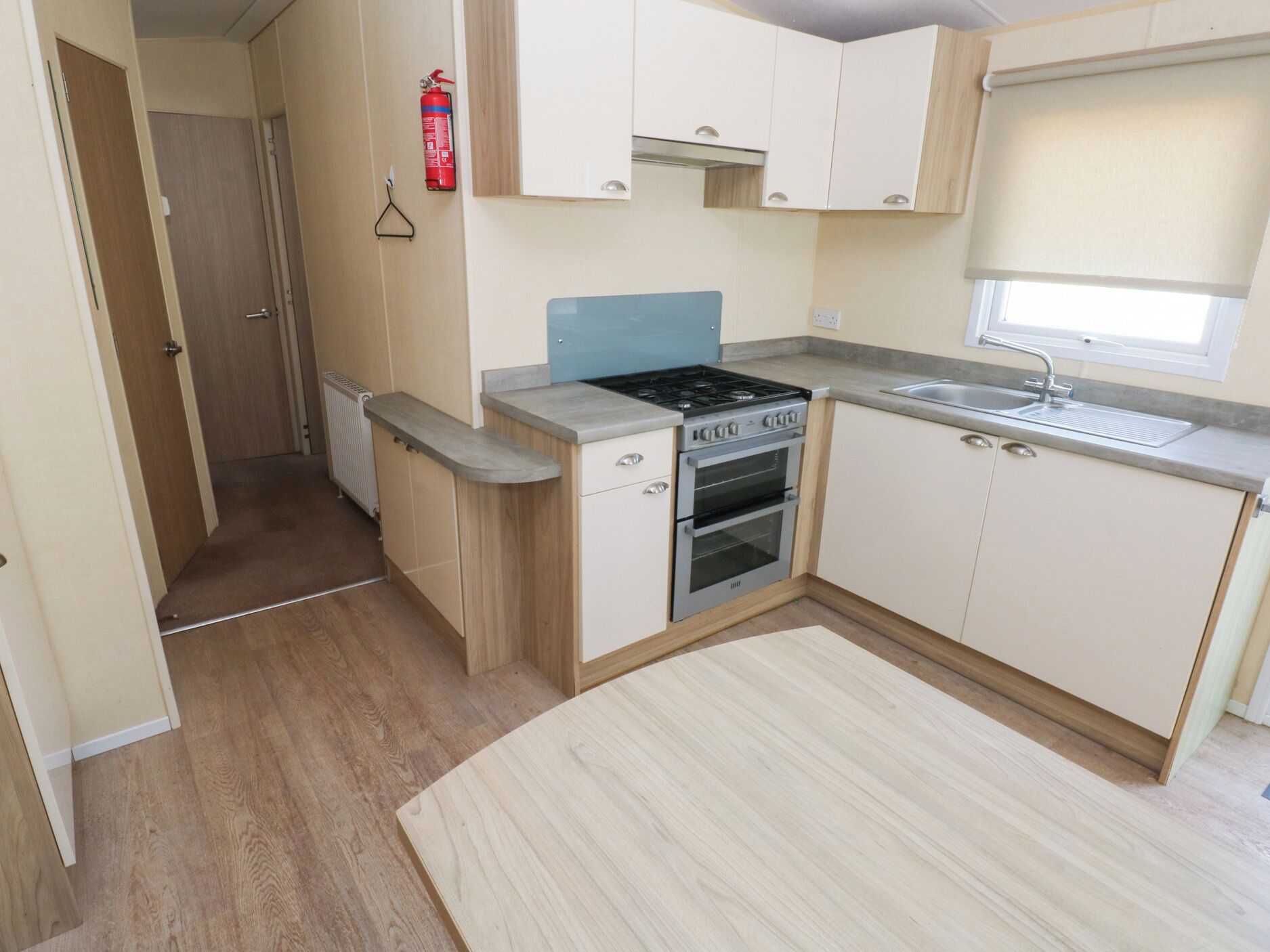 A compact kitchen with a stove, oven, and sink. There is a wooden cabinet and a small window with a blind.