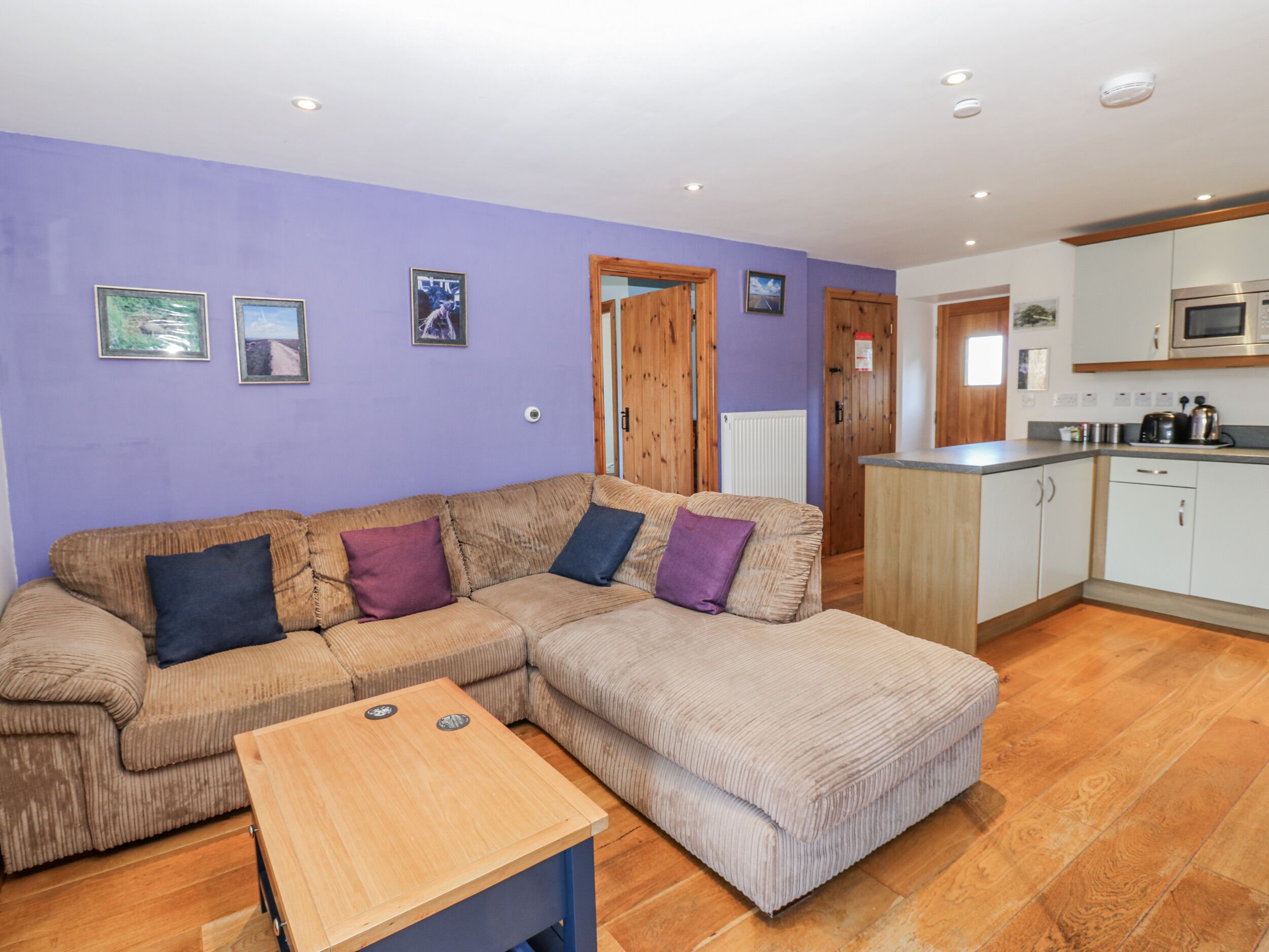 A living room with a sectional sofa, a wooden coffee table, and a kitchen area with cabinets and appliances.