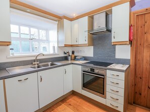 A modern kitchen with white cabinets, a stainless steel sink, and a built-in oven. - Swallows Rest (Hexham)