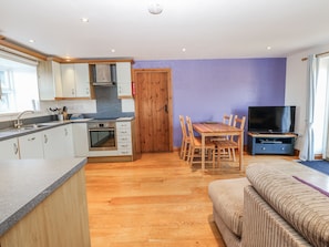 A modern kitchen with a built-in oven and sink, wooden dining table with chairs, and a flat-screen TV on a stand. - Swallows Rest (Hexham)