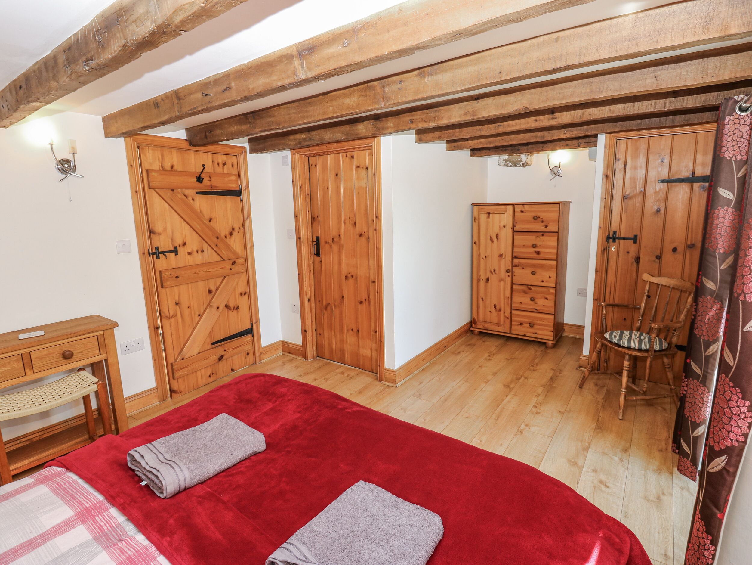 Une chambre avec un plancher en bois, une moquette rouge, une armoire en bois, une chaise en bois et un lit en bois.