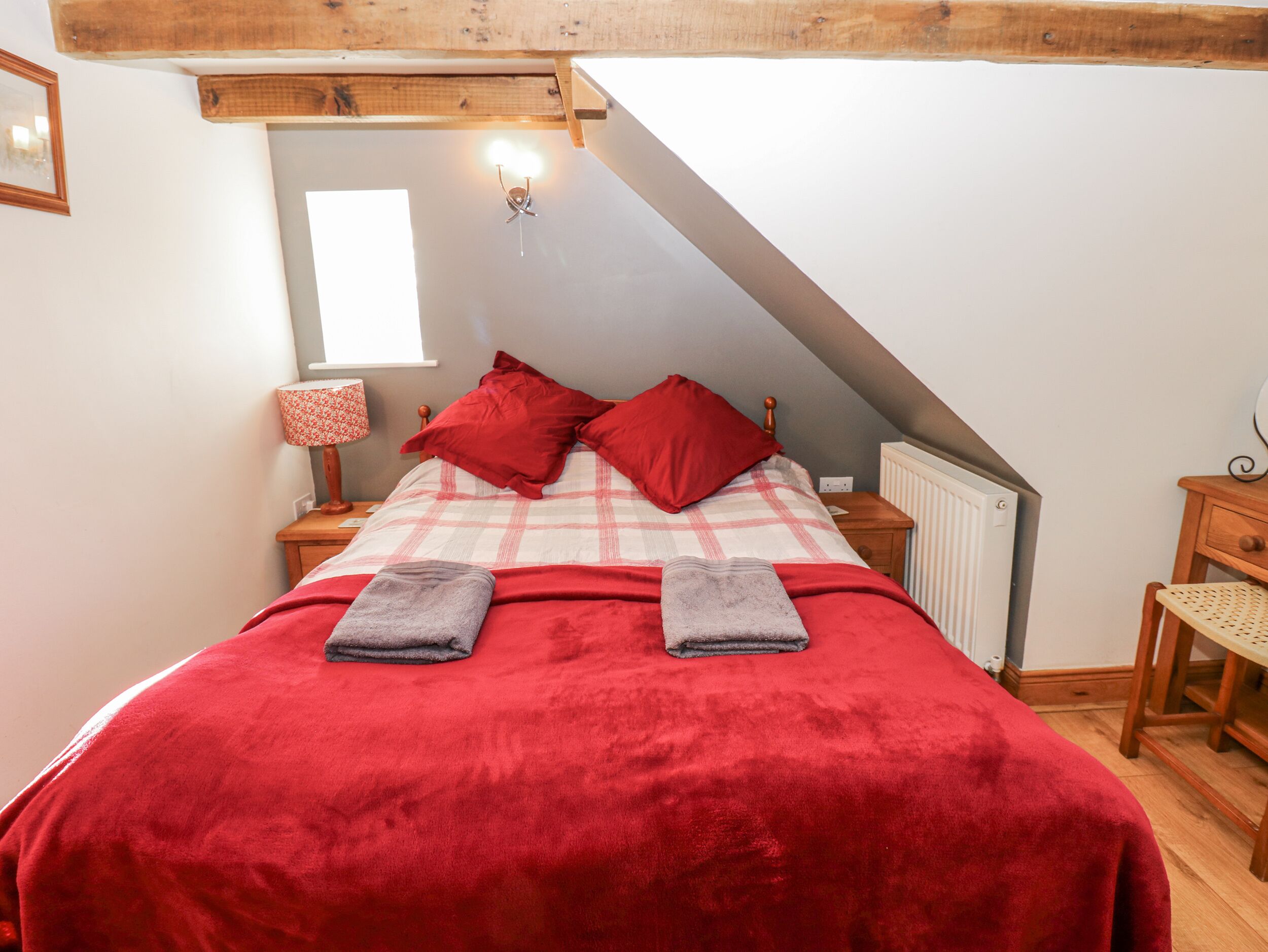 Una camera da letto con soffitto spiovente, un letto con biancheria rossa, un comodino con una lampada e un termosifone.
