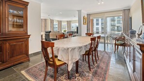 A spacious dining area with a large round table, wooden chairs, and a patterned rug.