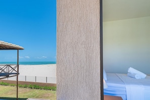 A room with a bed, a view of the beach, and a covered area with a railing.