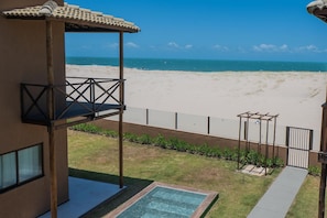 A beach view from a covered outdoor area with a pool and a pergola.