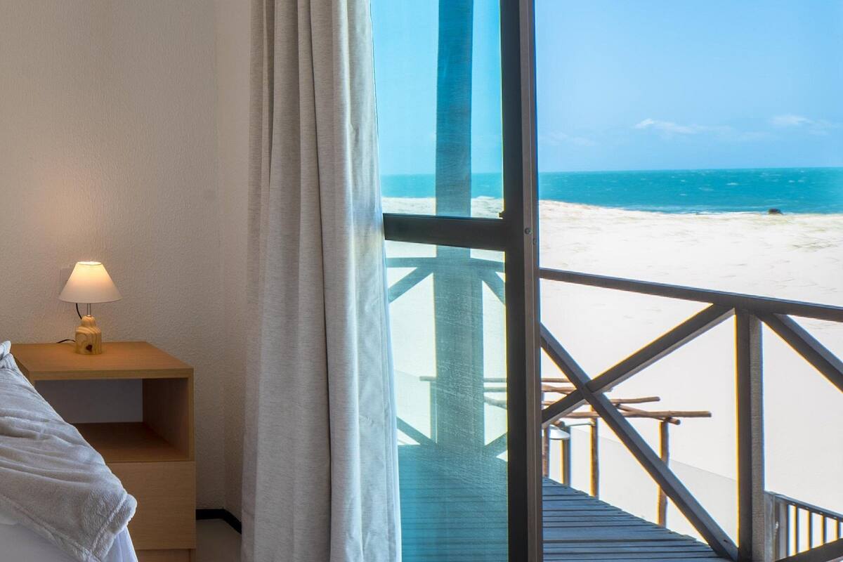 Une chambre avec un lit, une table de chevet avec une lampe et une grande fenêtre donnant sur une plage.