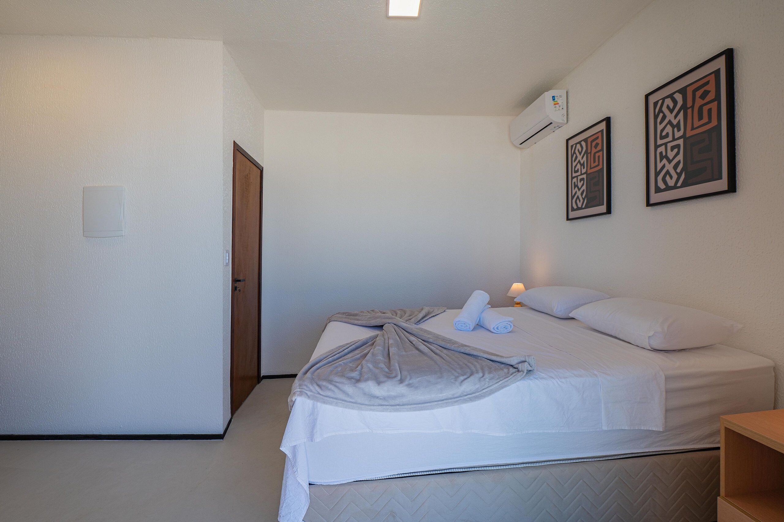 A hotel room with a bed, a wooden door, and two framed wall art pieces.