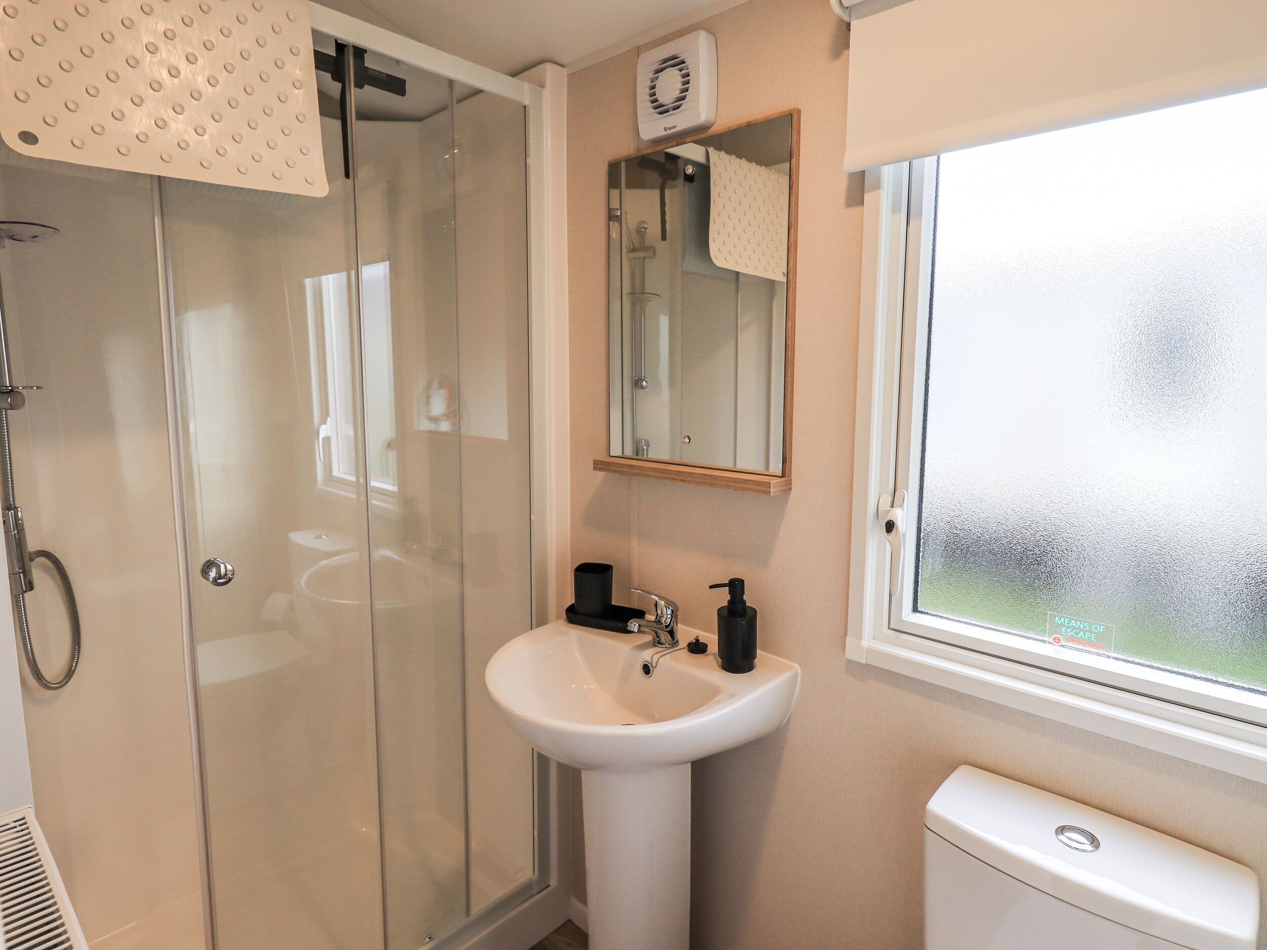 A bathroom with a glass shower enclosure, a white sink, a mirror, and a window.