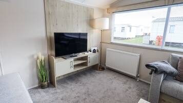 Una sala de estar con televisor de pantalla plana, una lámpara, un radiador y una ventana con persianas.