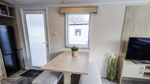 Una cocina compacta con una mesa de madera, asientos tipo banco, una pequeña planta en maceta y un televisor sobre un mueble.