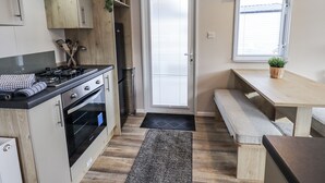 Una cocina compacta con estufa, horno y armarios de madera. Incluye un banco y una pequeña mesa con una planta.