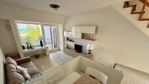 Een moderne woonkamer met een bank, een eettafel met placemat en een keukenhoek met televisie en kastjes.