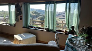 Una habitación con vistas a colinas ondulantes, un banco de madera, una mesa con un jarrón y una pared decorada con platos.