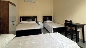 A room with three single beds, a desk with a chair, and a small refrigerator.
