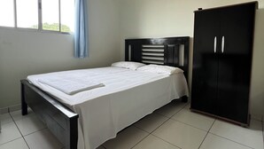 A bedroom with a bed, a wardrobe, a window with curtains, and an air conditioning unit.