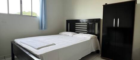 A bedroom with a bed, a wardrobe, a window with curtains, and an air conditioning unit.