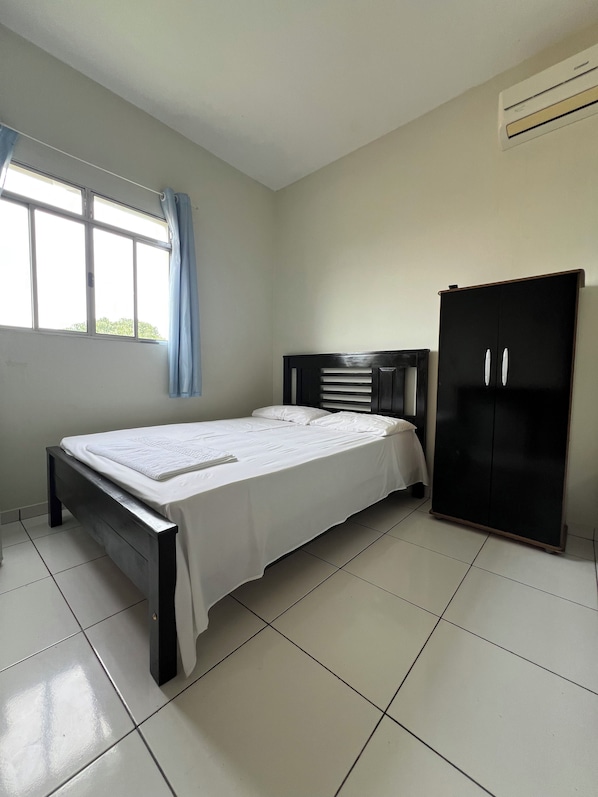 A bedroom with a bed, a wardrobe, a window with curtains, and an air conditioning unit.