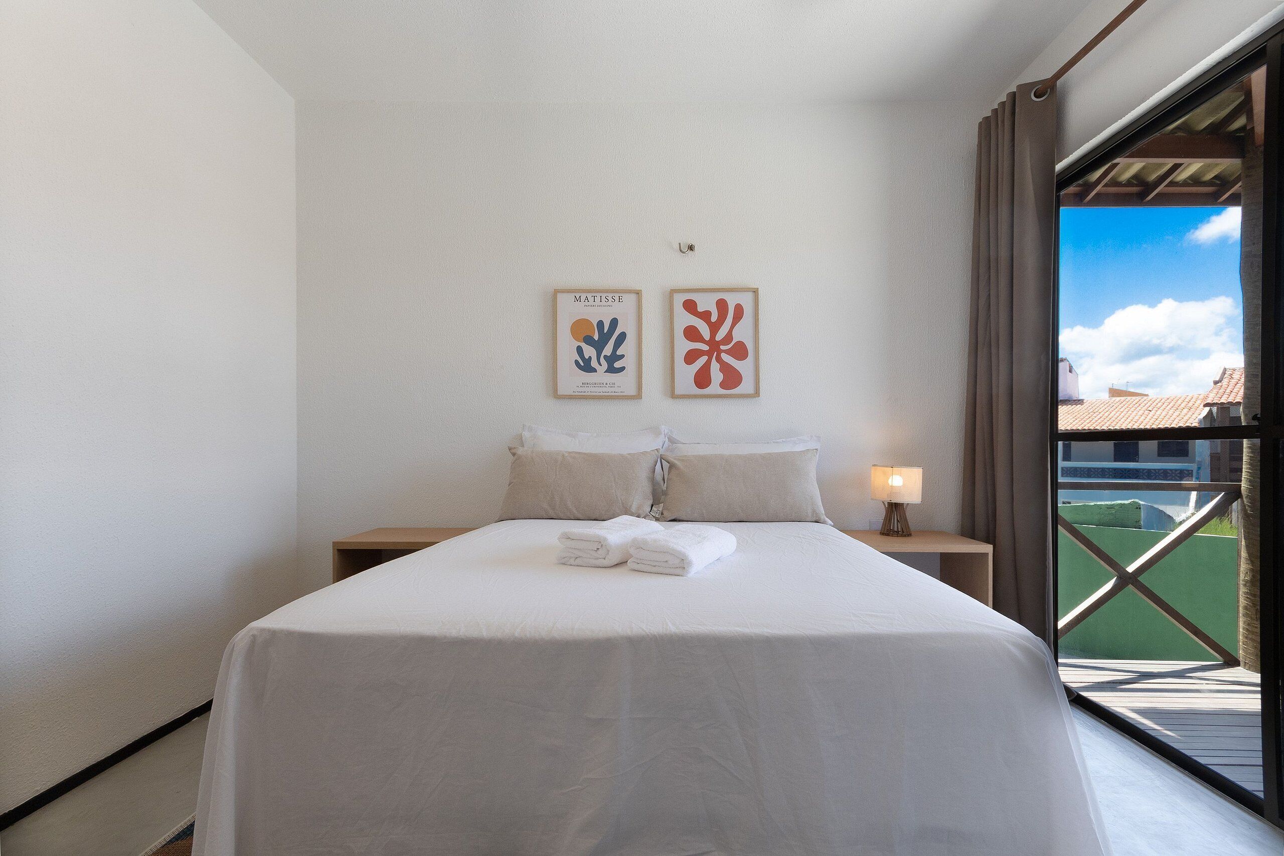 Una cama bien hecha con ropa blanca y dos cuadros en la pared.