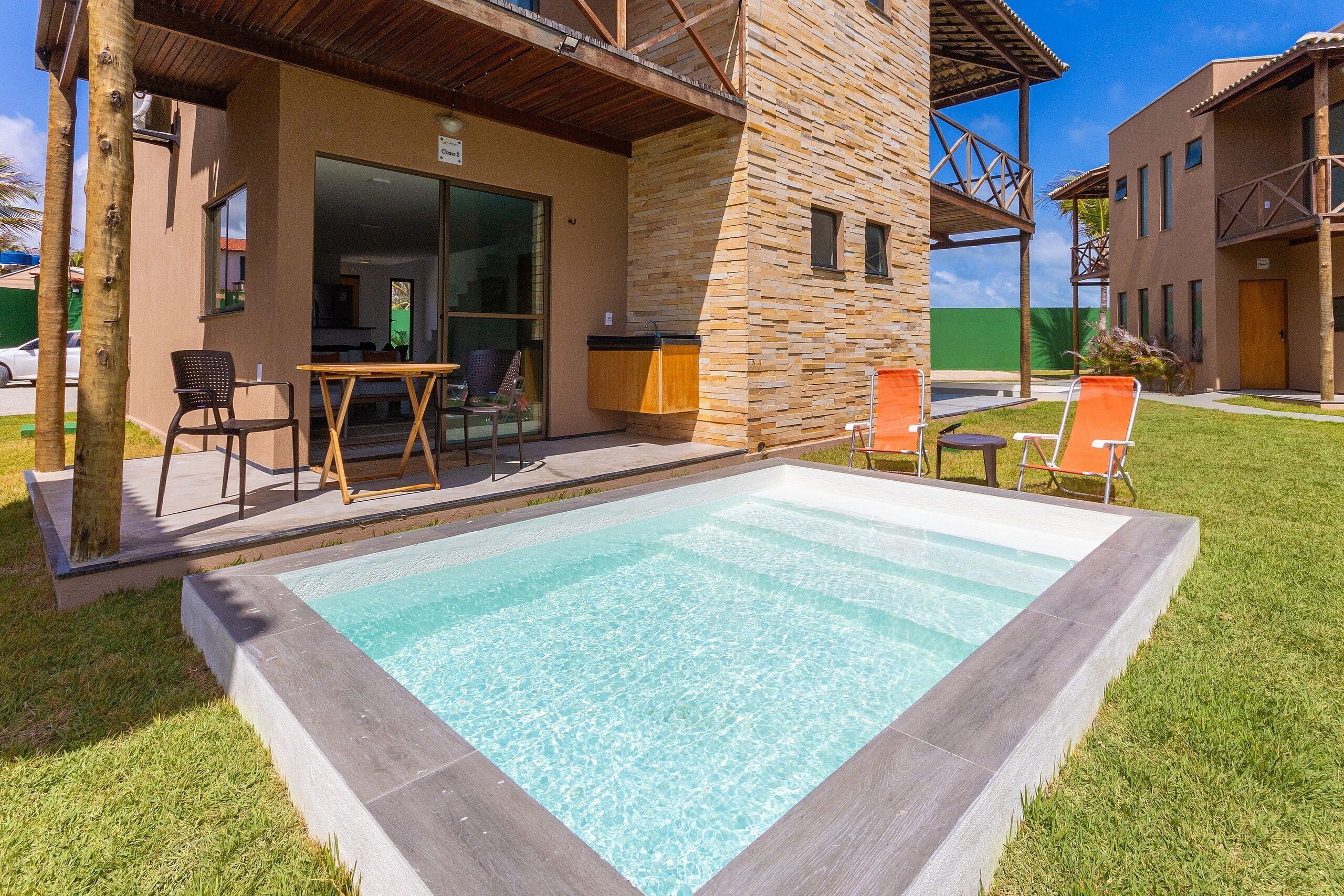 A swimming pool with a stone wall and a covered seating area with chairs.